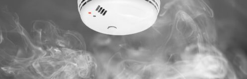 White smoke detector mounted on ceiling with wisps of white smoke curling toward it