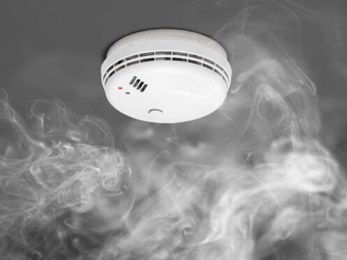 White smoke detector mounted on ceiling with wisps of white smoke curling toward it